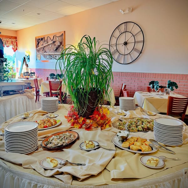 A restaurant buffet table laden with various appetizers, desserts, and stacks of plates.