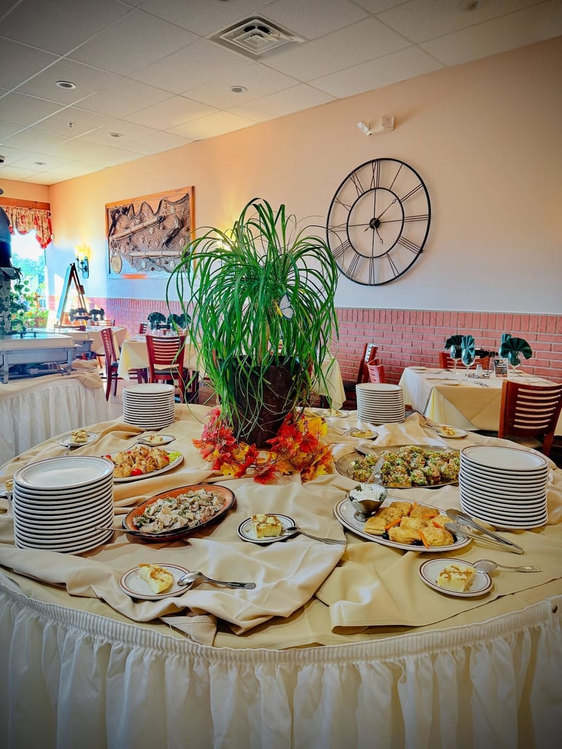 A restaurant buffet table laden with various appetizers, desserts, and stacks of plates.